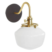 Wall sconce with dark round backplate, brushed brass arm, and clear glass globe